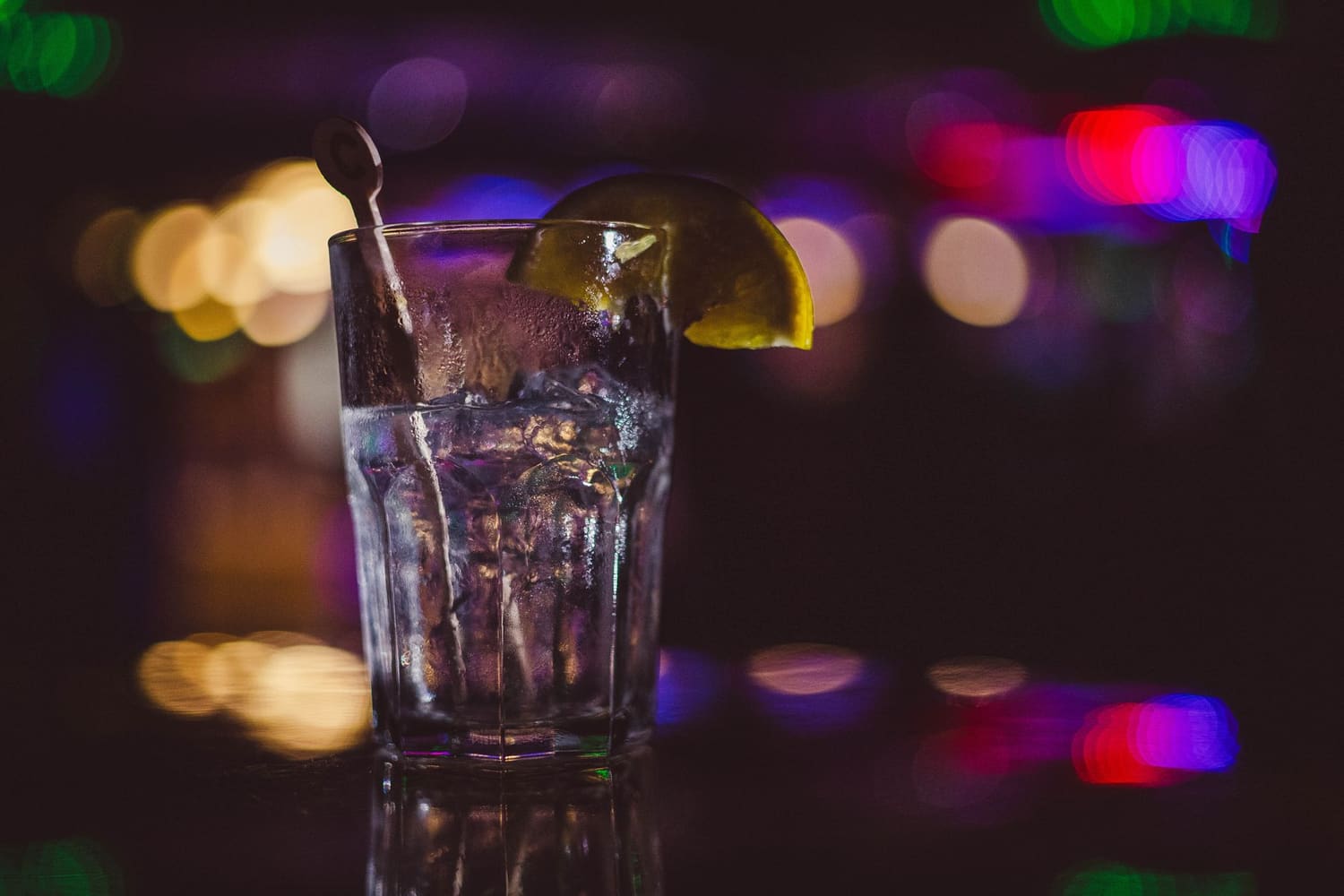 Copo com gelo e lima ao balcão de um bar, com luzes de néon desfocadas ao fundo