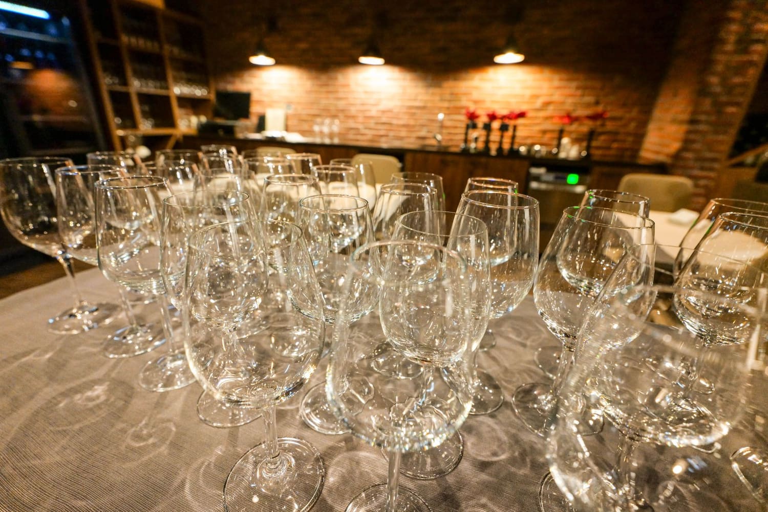 Fila de copos de vinho alinhados ao balcão de um bar com luz quente