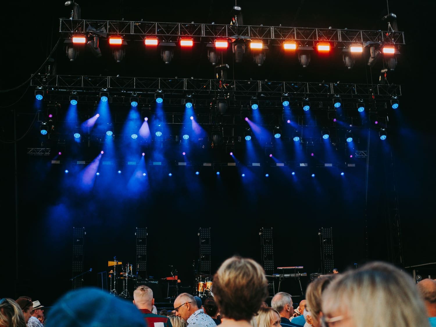 Público em frente a um palco pequeno, com luzes coloridas, num concerto noturno